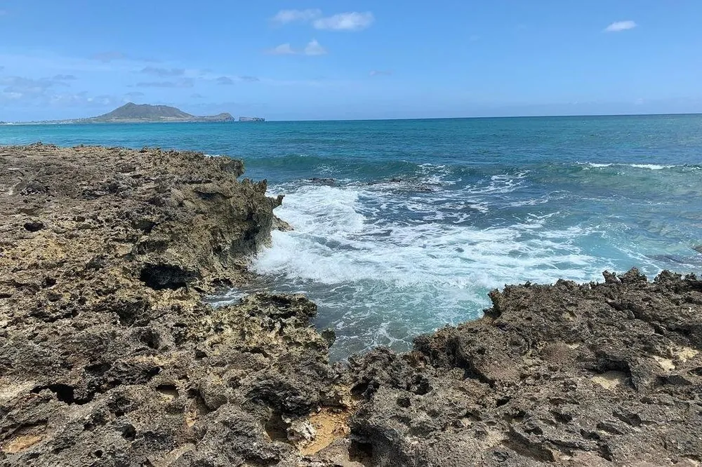 Una orilla de roca áspera y picada con olas rompiendo en un hueco y, al otro lado del agua, el promontorio de una isla